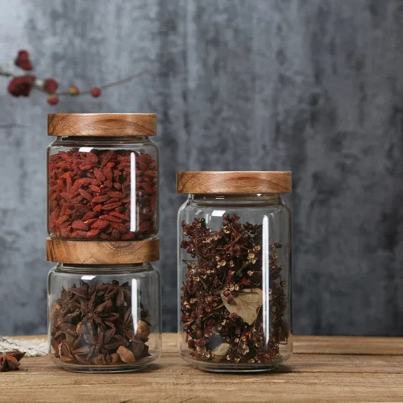 Two wooden-lid jars holding goji berries and star anise on a wooden board